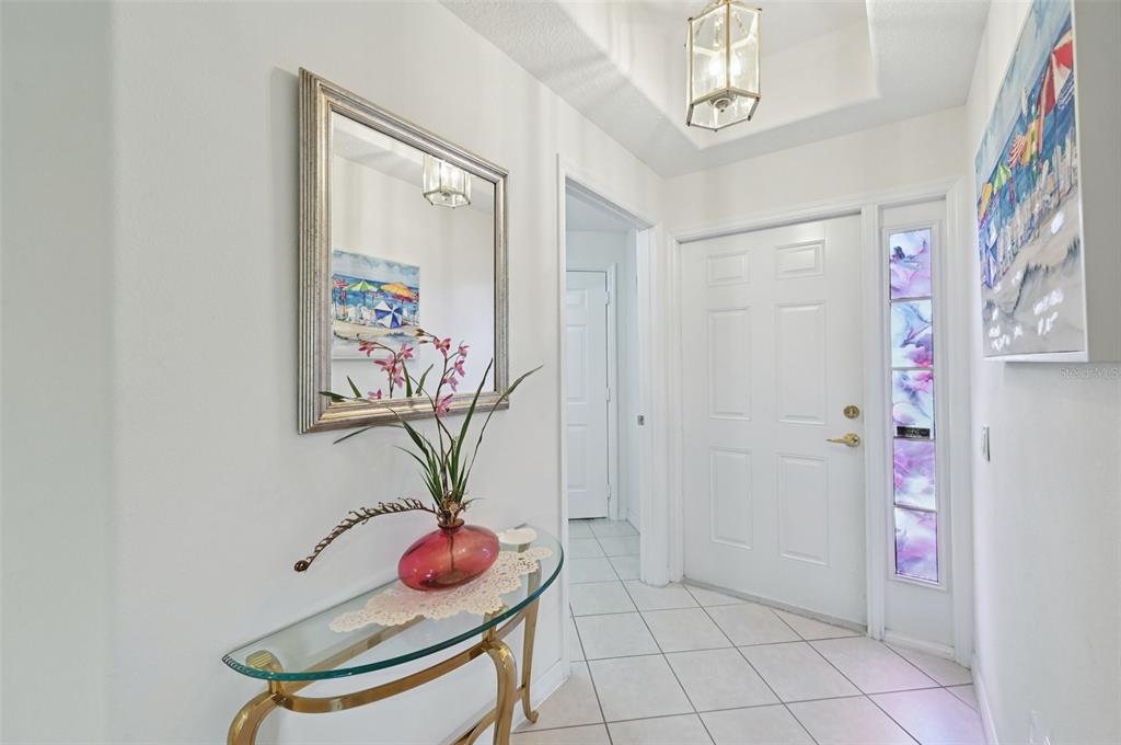 A bright entryway features a glass console table, a wall mirror, and a white door — 7050 PROSPERITY CIRCLE UNIT 904, SARASOTA, FL