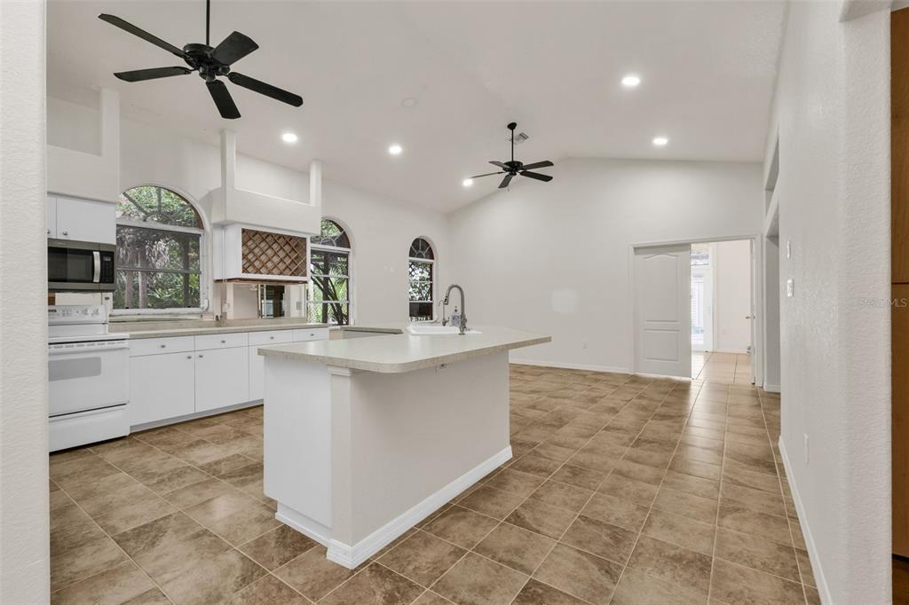 A white kitchen with an island, tile flooring, and vaulted ceilings with two ceiling fans — 4056 GINGOLD STREET, PORT CHARLOTTE, FL