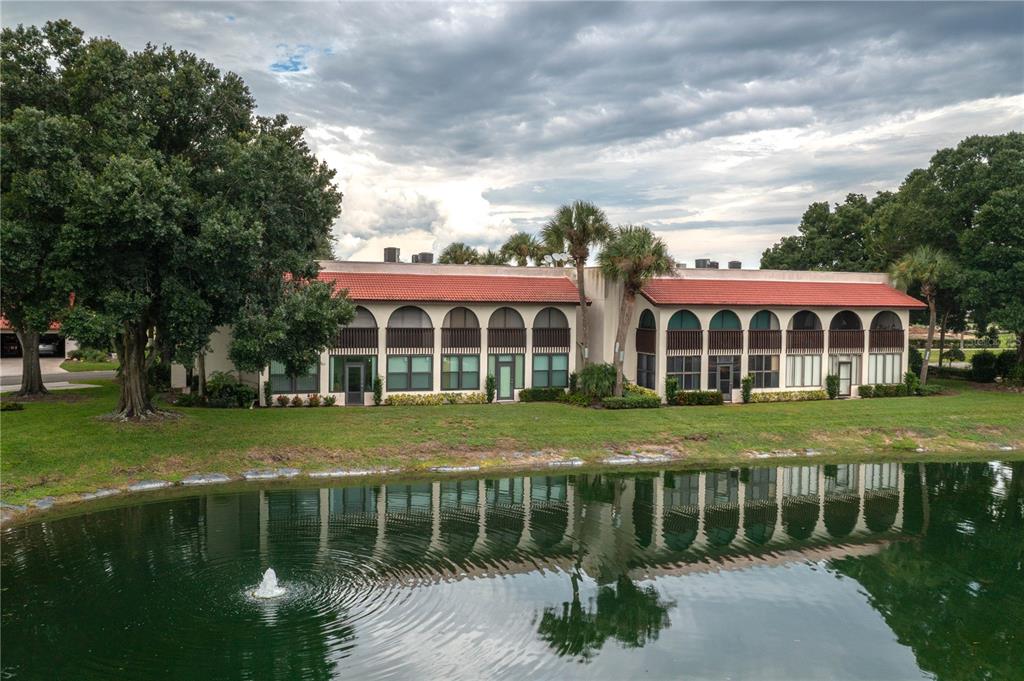 A two-story building with arched windows sits beside a pond with a fountain — 8203 VILLAGE DRIVE UNIT H-23, LAKE WALES, FL