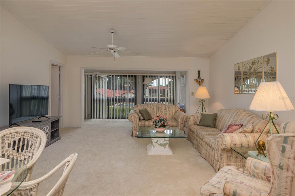A living room features beige carpeting, floral sofas, a glass coffee table, and sliding glass doors — 8203 VILLAGE DRIVE UNIT H-23, LAKE WALES, FL