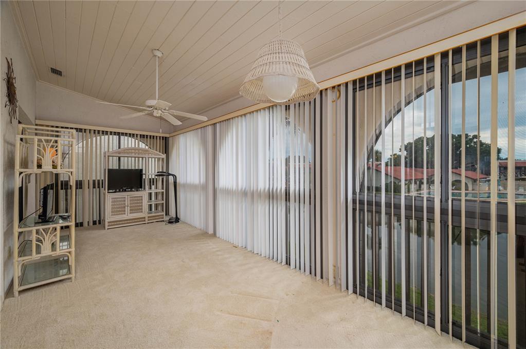 A sunroom with beige carpet, a ceiling fan, a wicker pendant light, and vertical blinds — 8203 VILLAGE DRIVE UNIT H-23, LAKE WALES, FL