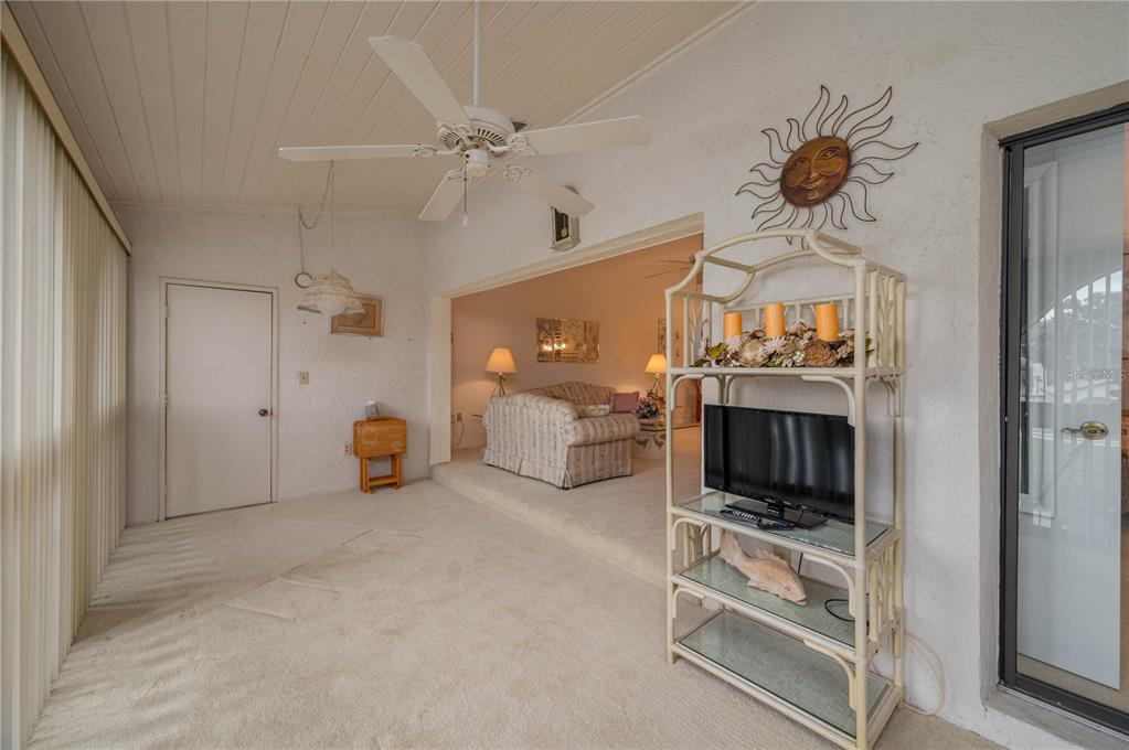 A carpeted sunroom with a ceiling fan opens into a living room with a sofa — 8203 VILLAGE DRIVE UNIT H-23, LAKE WALES, FL