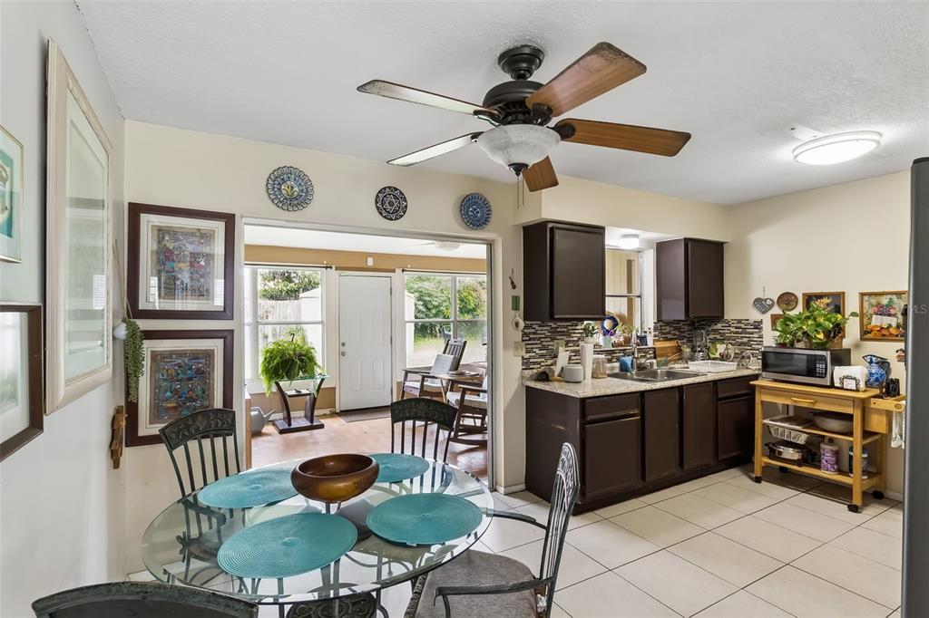 A kitchen and dining area with dark cabinets, a glass table, and a sunroom beyond — 120 MILTA LANE, KISSIMMEE, FL