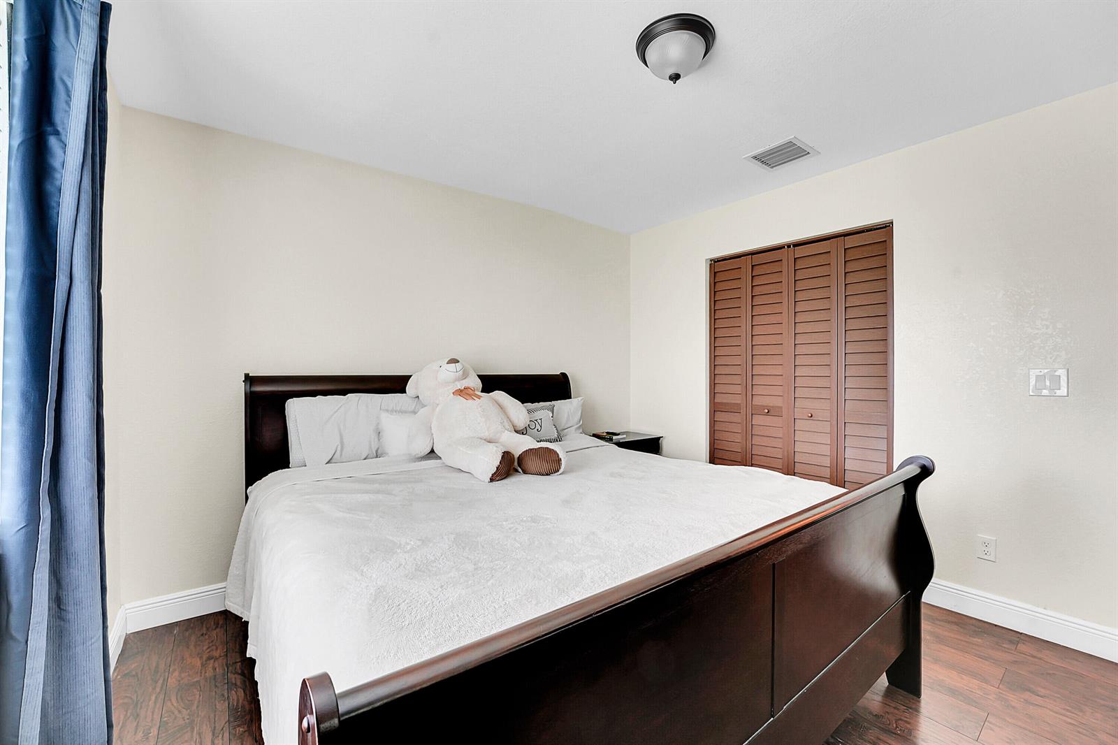 A bedroom features a dark wood sleigh bed, white bedding, and brown louvered closet doors — 2856 Harson Way, Fort Pierce FL 34946, FORT PIERCE, FL
