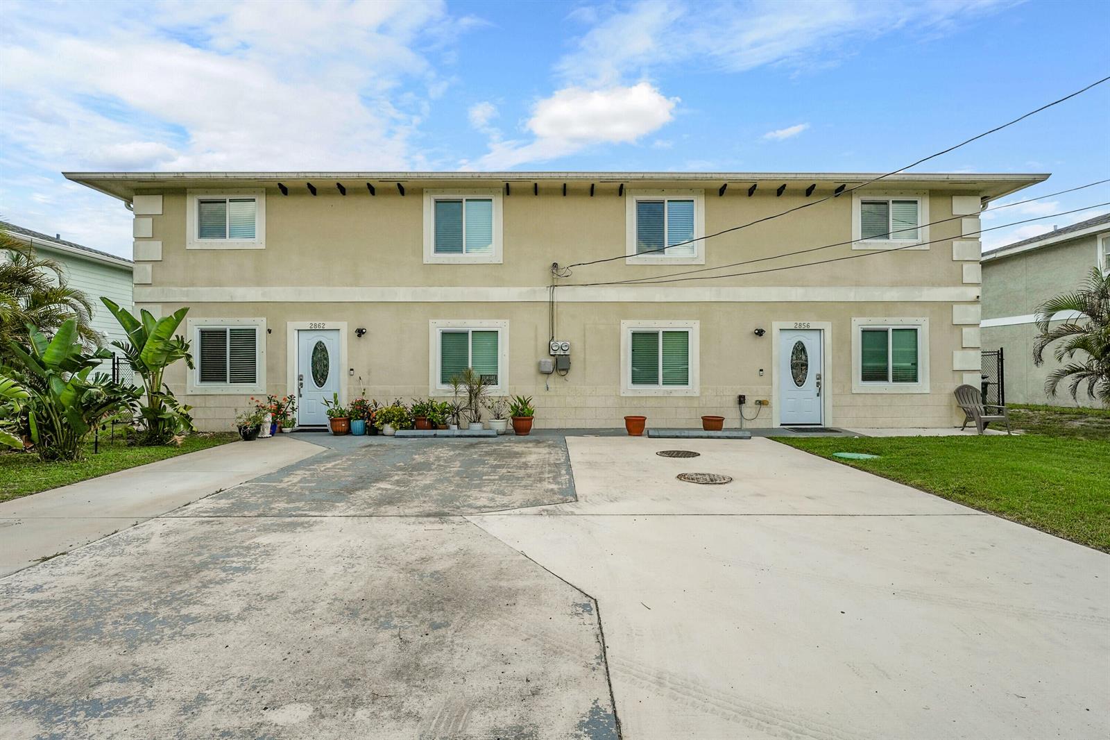 A two-story duplex with a concrete driveway, white doors, and several potted plants — 2856 Harson Way, Fort Pierce FL 34946, FORT PIERCE, FL