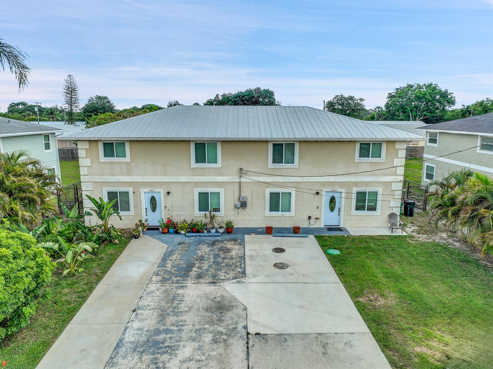 A two-story duplex with a metal roof, beige stucco exterior, and a shared concrete driveway — 2856 Harson Way, Fort Pierce FL 34946, FORT PIERCE, FL