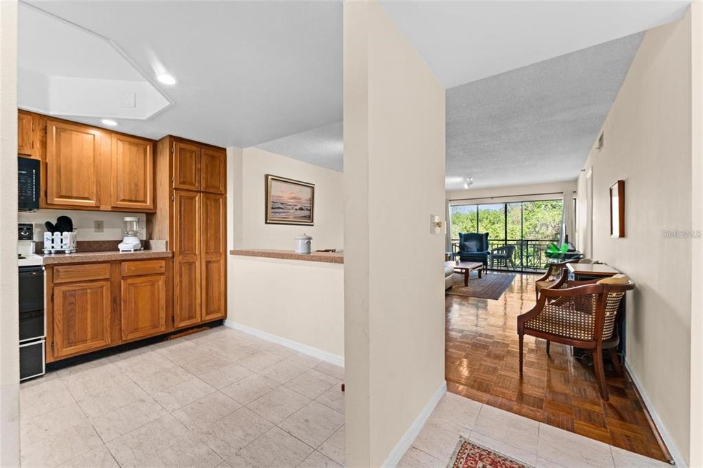 A kitchen with wood cabinets and tile floors opens into a living area with parquet flooring — 1162 CARMEL CIRCLE UNIT 440, CASSELBERRY, FL