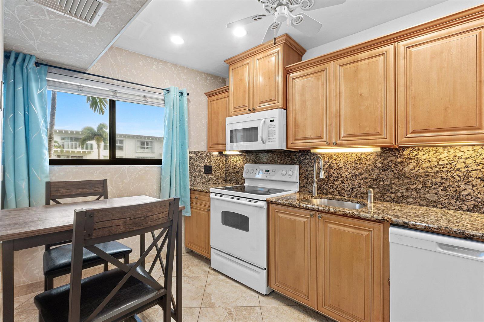 A kitchen with light wood cabinets, granite countertops, a white stove, and a dining area — 3605 S Ocean Boulevard, South Palm Beach FL 33480, SOUTH PALM BEACH, FL
