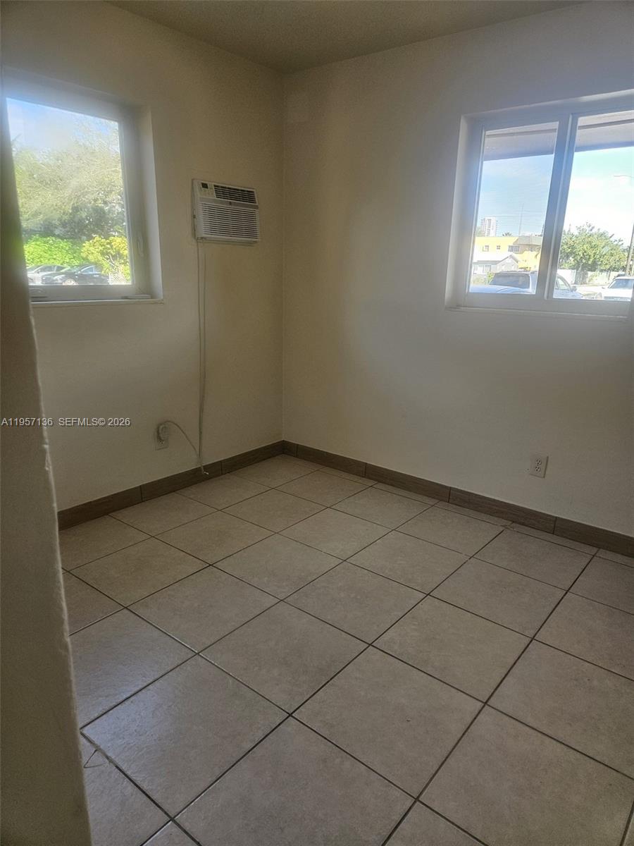 An empty room features beige tile flooring, two windows, and a wall-mounted air conditioner — 2230 Madison St # 01, Hollywood FL 33020, HOLLYWOOD, FL