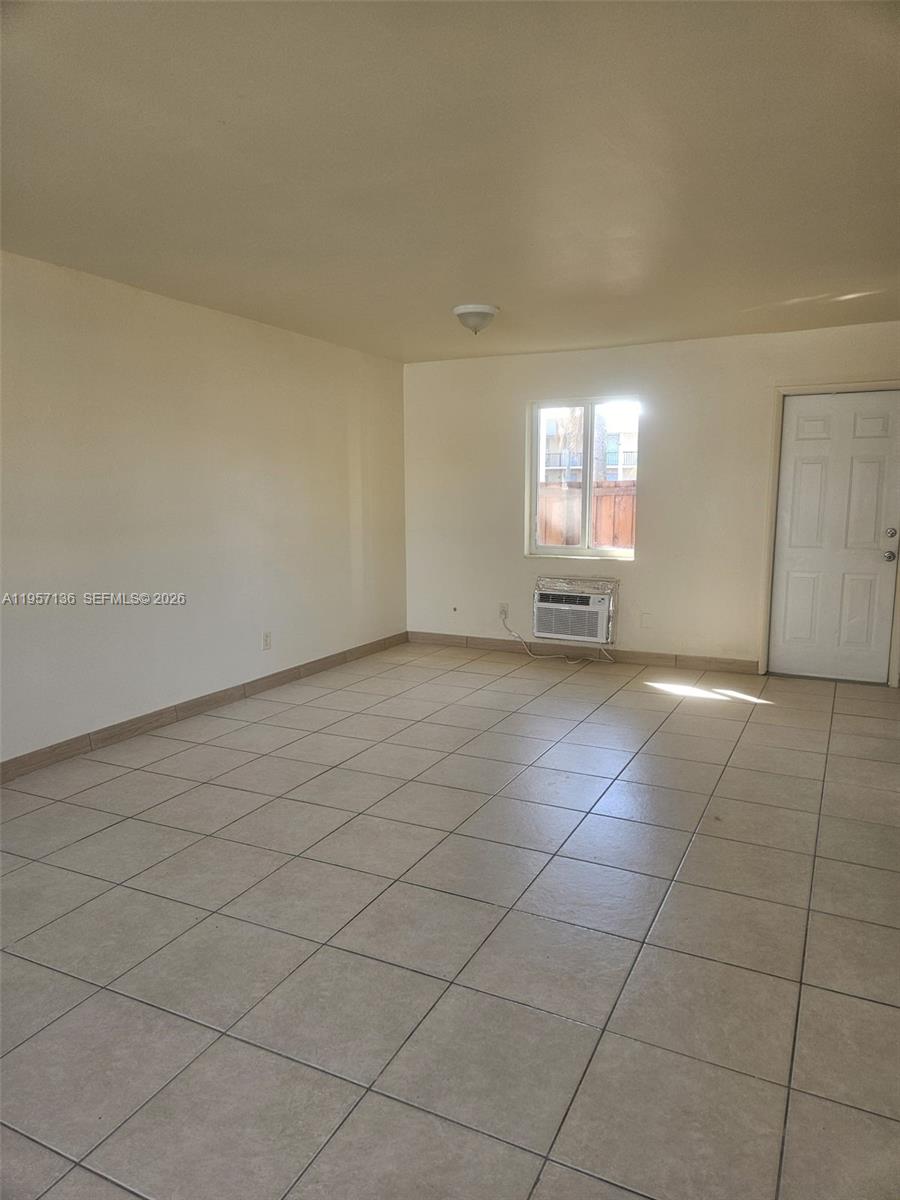 An empty room features beige tile flooring, a window air conditioning unit, and a white door — 2230 Madison St # 01, Hollywood FL 33020, HOLLYWOOD, FL