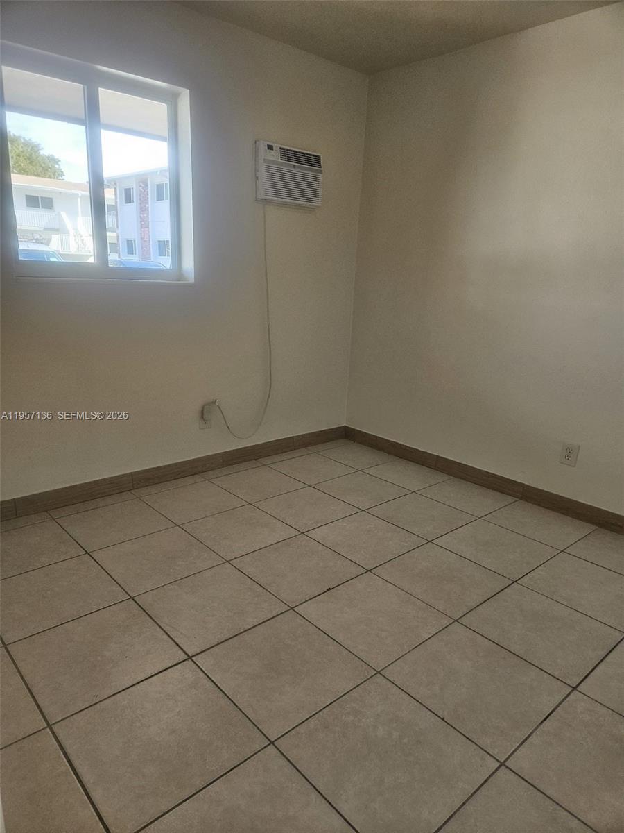 A room with beige tile flooring, a window, and a wall-mounted air conditioning unit — 2230 Madison St # 01, Hollywood FL 33020, HOLLYWOOD, FL