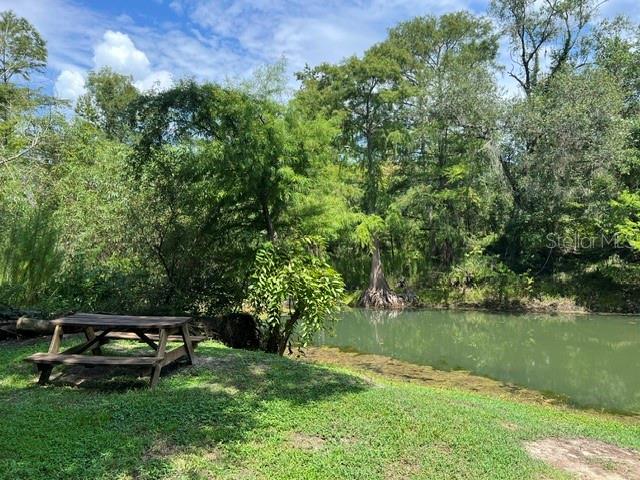 A wooden picnic table sits on a grassy bank beside a calm, tree-lined river — 39849 STATE ROAD 575, DADE CITY, FL