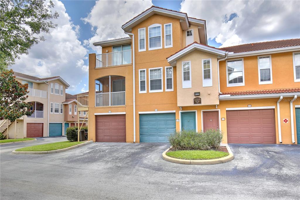 The exterior of a multi-story townhouse complex features orange stucco walls and several garage doors — 12203 WILD IRIS WAY UNIT 104, ORLANDO, FL