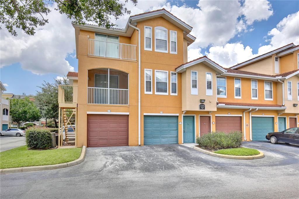 An exterior view of a multi-story townhouse complex with garages and balconies under a cloudy sky — 12203 WILD IRIS WAY UNIT 104, ORLANDO, FL
