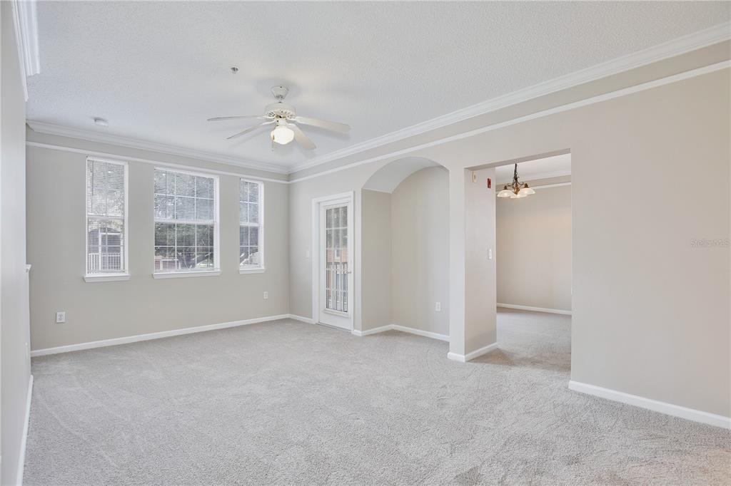 A carpeted living room features a ceiling fan, crown molding, and a glass-paned exterior door — 12203 WILD IRIS WAY UNIT 104, ORLANDO, FL