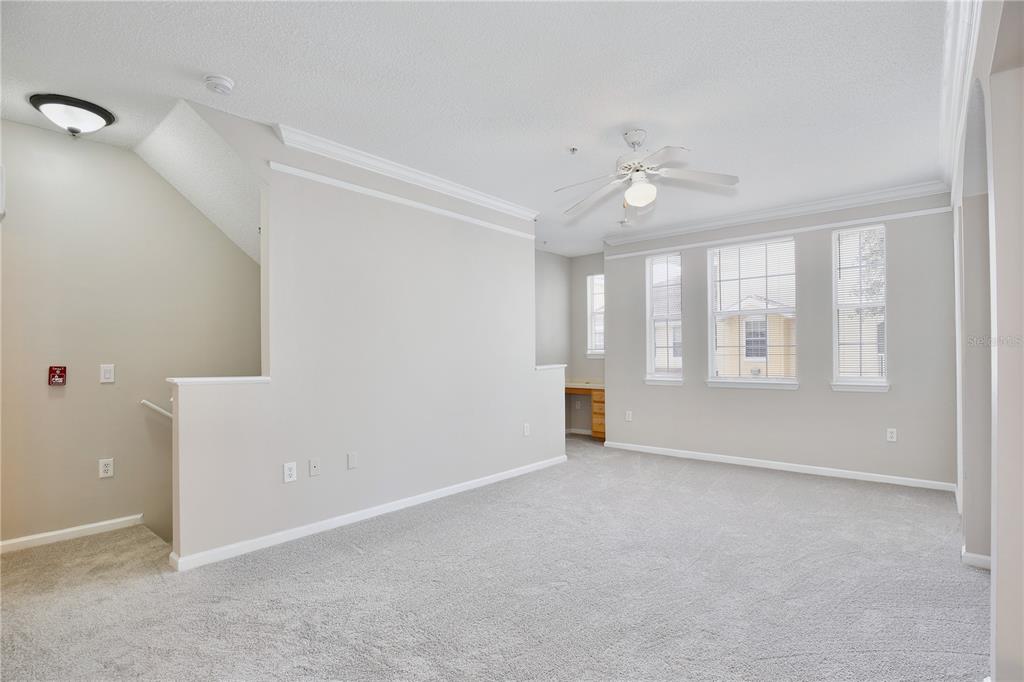 A carpeted room with a ceiling fan, a half-wall, and a built-in desk area — 12203 WILD IRIS WAY UNIT 104, ORLANDO, FL
