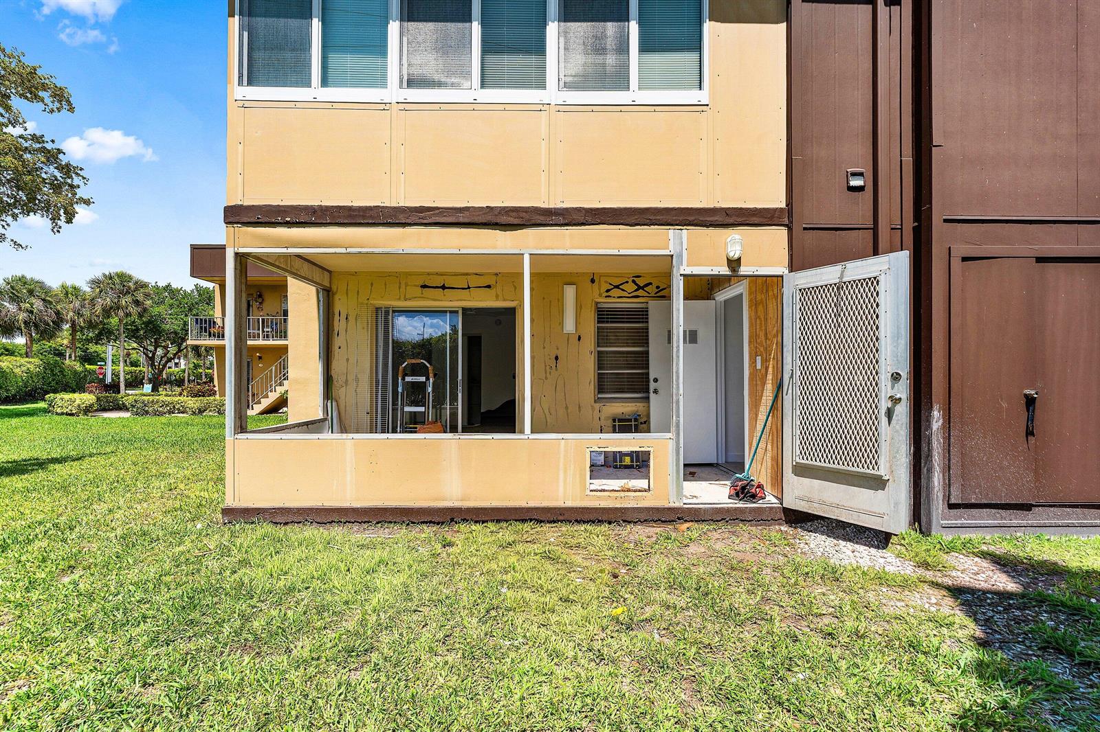 An exterior view of a ground-floor screened-in patio with a metal door and beige siding — 790 Burgundy Q, Delray Beach FL 33484, DELRAY BEACH, FL