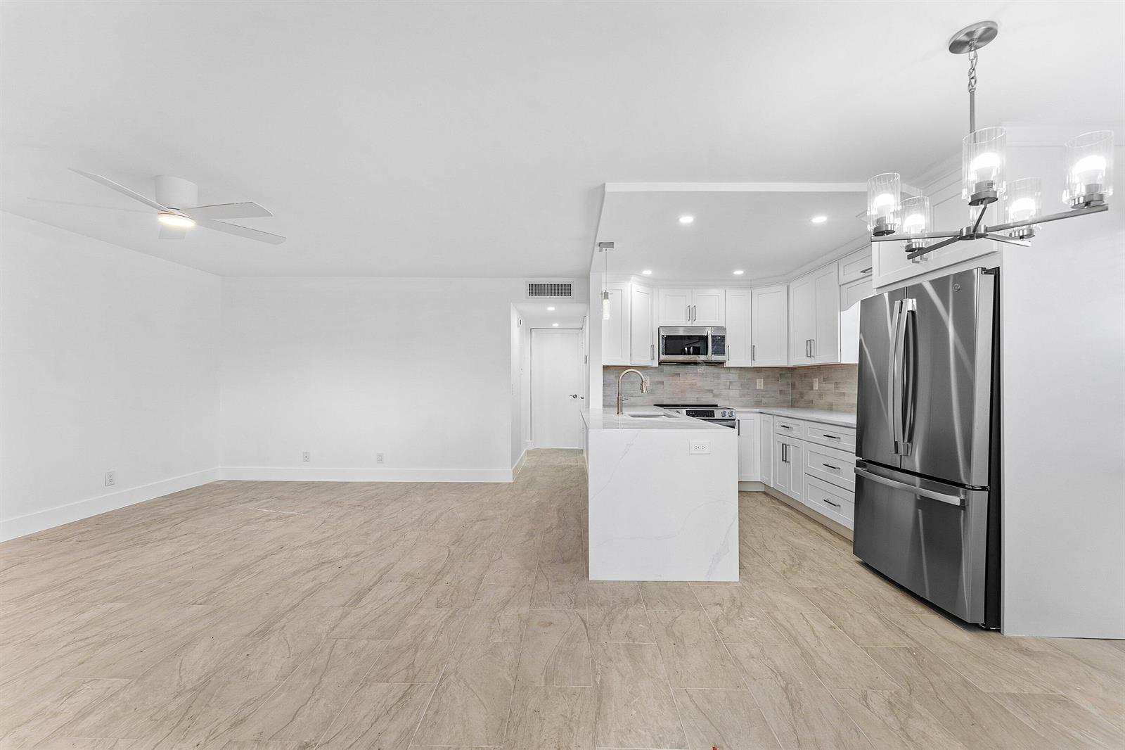 A modern kitchen with white cabinets and a marble island opens to a living area — 790 Burgundy Q, Delray Beach FL 33484, DELRAY BEACH, FL