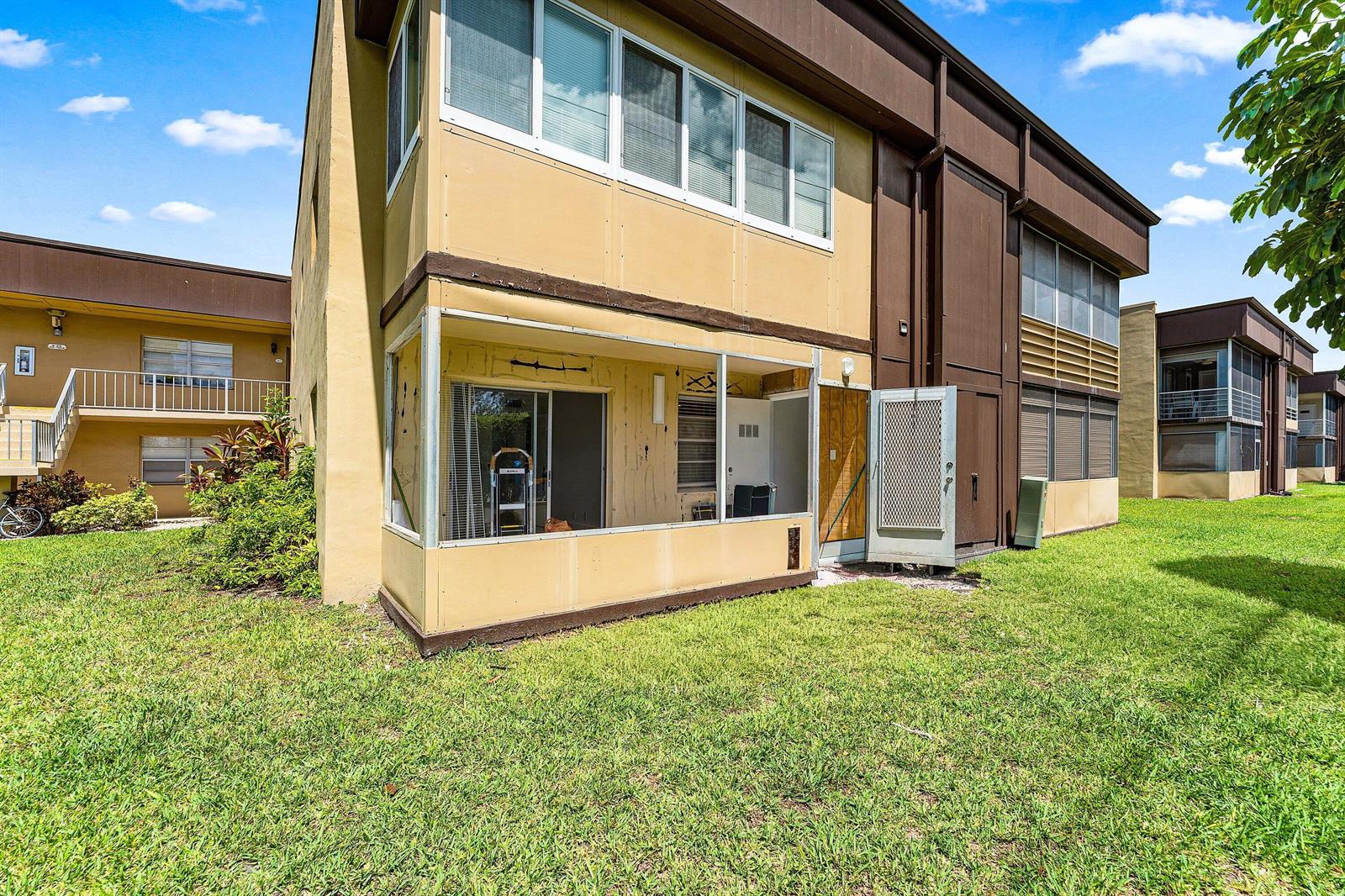 Exterior view of a two-story apartment building with a ground-level screened-in patio and lawn — 790 Burgundy Q, Delray Beach FL 33484, DELRAY BEACH, FL
