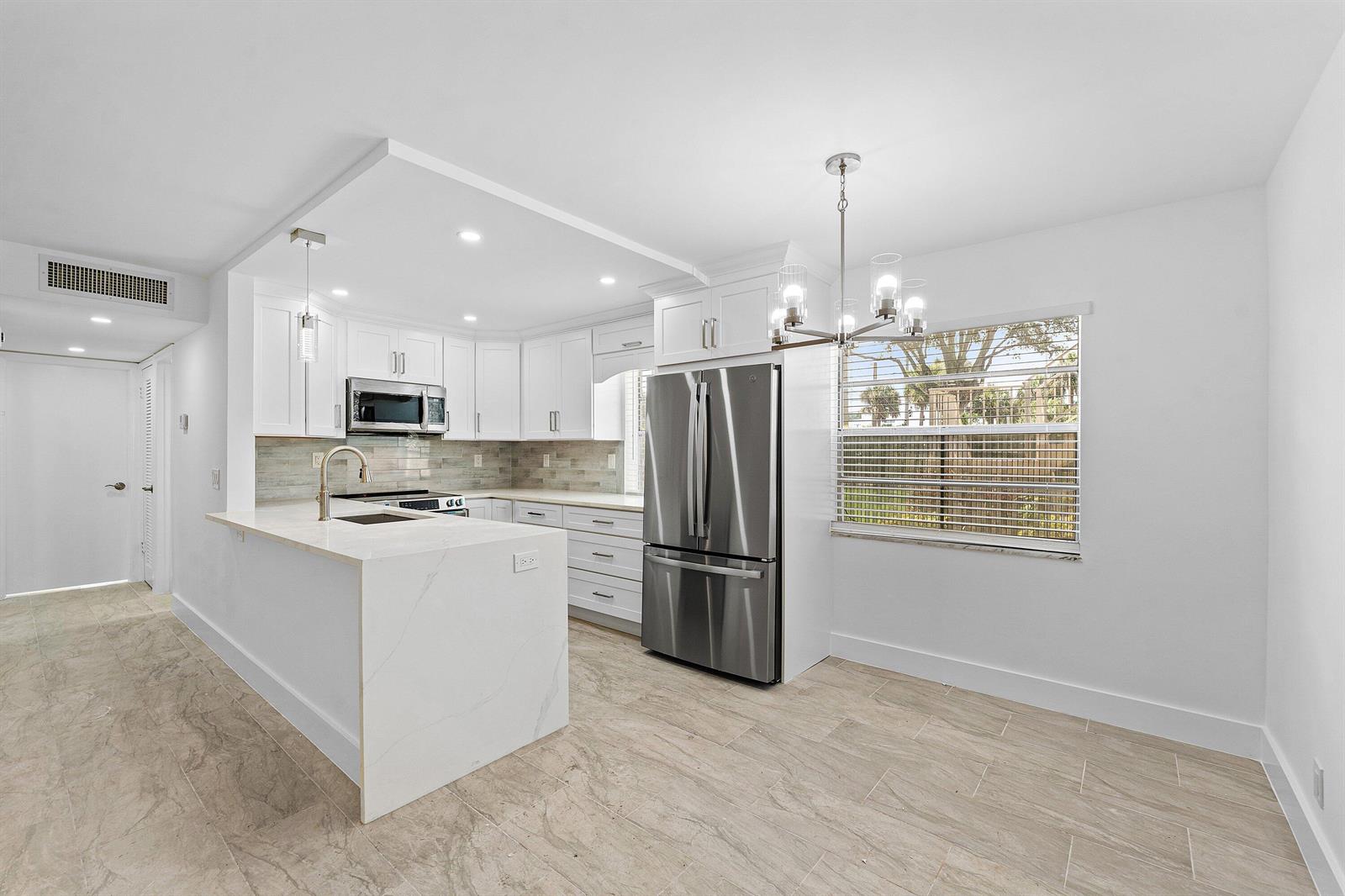 A modern kitchen features white cabinets, stainless steel appliances, a marble island, and tile flooring — 790 Burgundy Q, Delray Beach FL 33484, DELRAY BEACH, FL