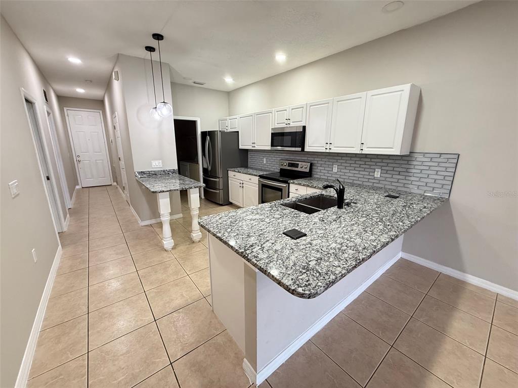 A kitchen features white cabinets, granite countertops, a tiled backsplash, and a breakfast bar — 3421 HOME TOWN LANE, ST CLOUD, FL
