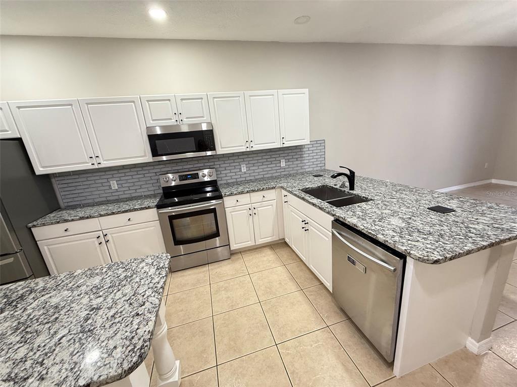 A kitchen features white cabinets, granite countertops, stainless steel appliances, and a gray tiled backsplash — 3421 HOME TOWN LANE, ST CLOUD, FL