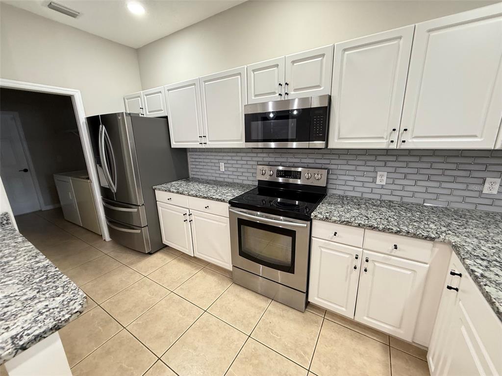 A kitchen features white cabinets, granite countertops, stainless steel appliances, and a gray subway tile backsplash — 3421 HOME TOWN LANE, ST CLOUD, FL