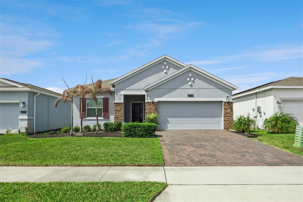 A single-story suburban house with a gray stucco exterior, stone accents, and a paved driveway — 2714 SLASH WAY, ST CLOUD, FL