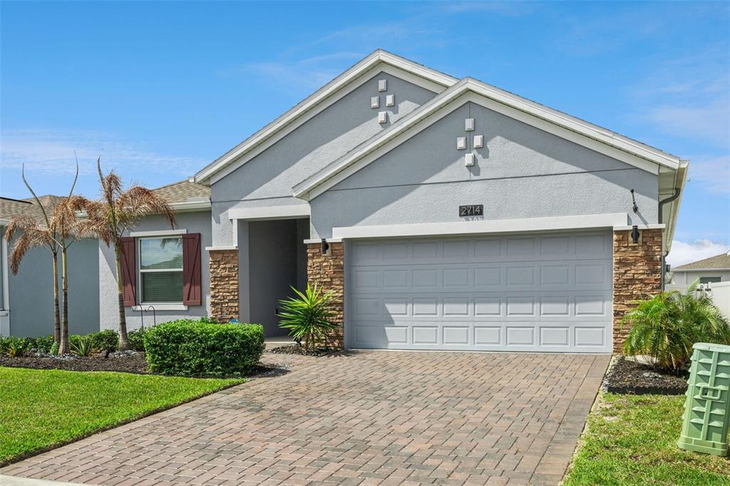 A single-story house with a gray stucco exterior, stone accents, and a paved driveway — 2714 SLASH WAY, ST CLOUD, FL