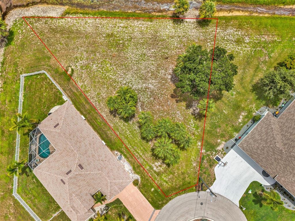An aerial view shows a vacant, triangular-shaped residential lot situated between two existing houses — 604 TRUMPET TREE, PUNTA GORDA, FL