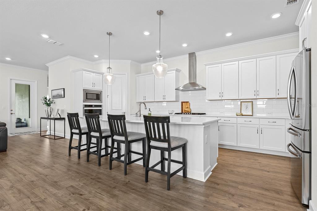 A modern kitchen features white cabinets, a large island with bar seating, and wood flooring — 13930 NATURES RESERVE DRIVE, LITHIA, FL