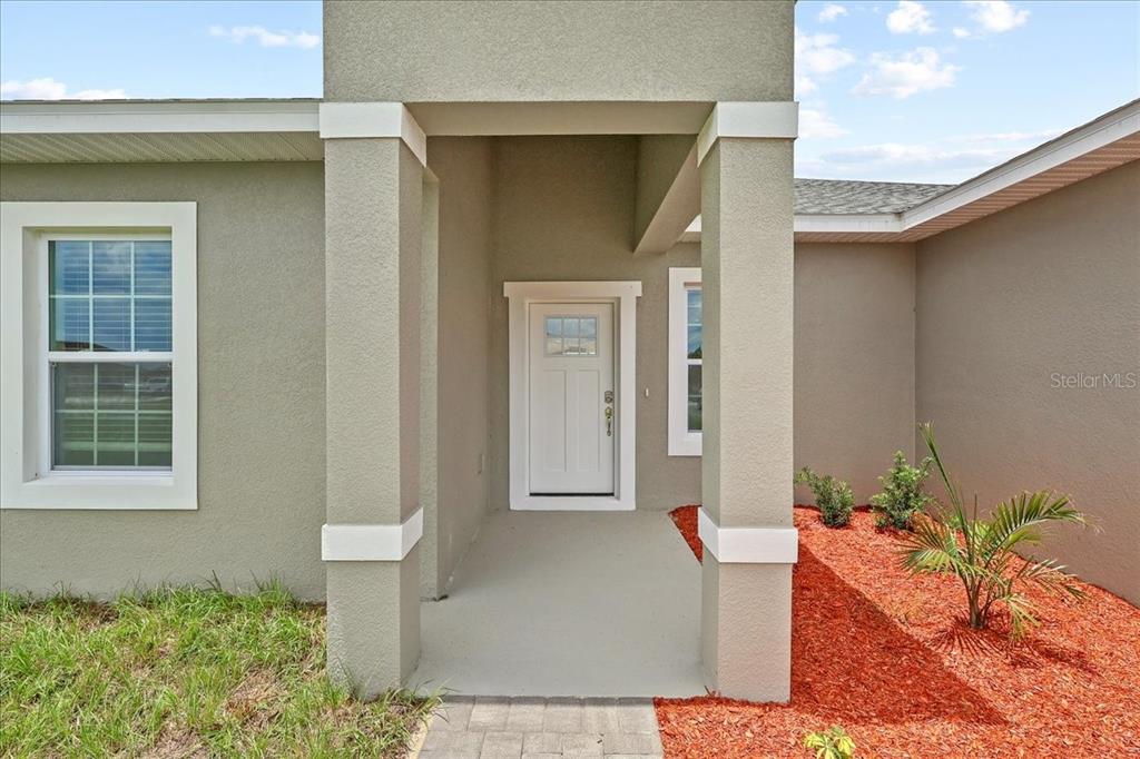 A covered entryway features a white front door, stucco walls, and a small palm tree — 2120 POINCIANA DRIVE, INDIAN LAKE ESTATES, FL