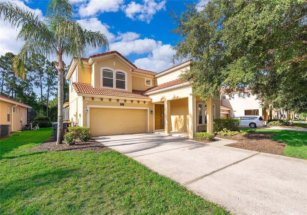 A two-story tan stucco house with a tile roof, garage, and driveway under a blue sky — 385 ORANGE COSMOS BOULEVARD, DAVENPORT, FL