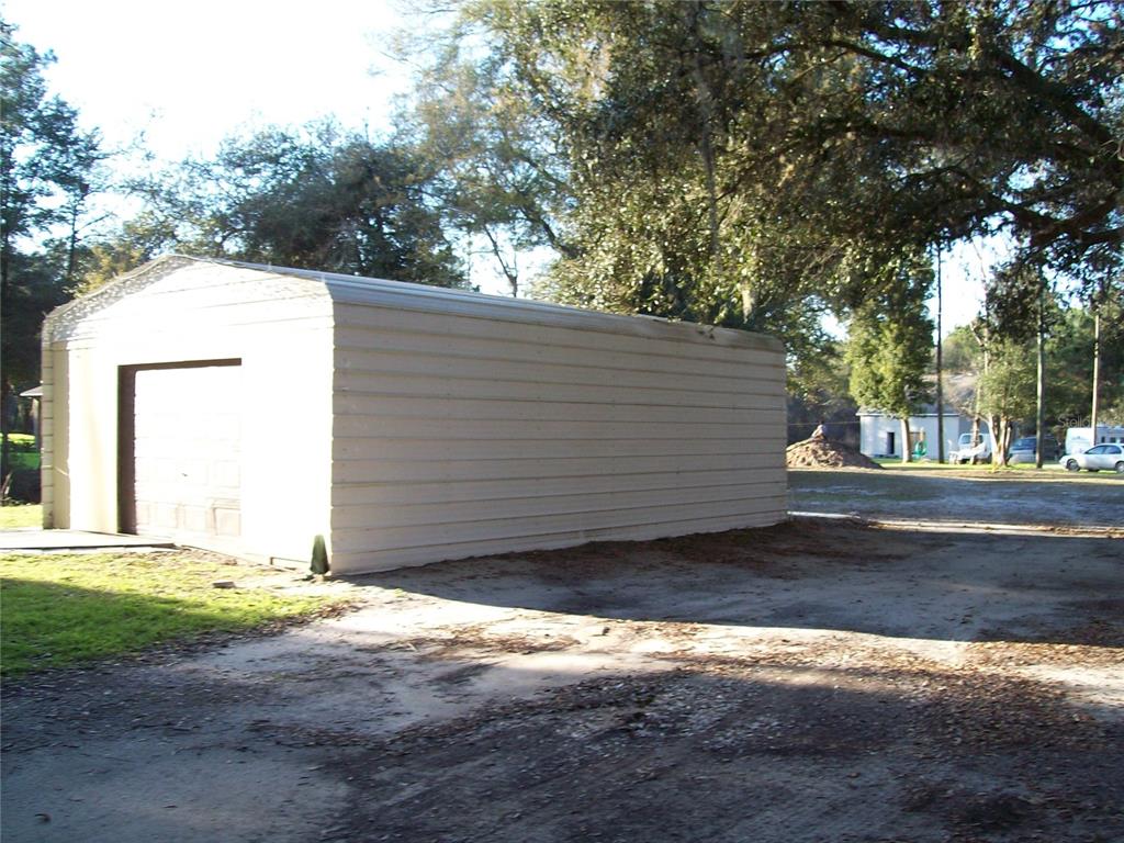 A detached metal garage sits on a dirt lot surrounded by trees — 6382 BAKER ROAD, KEYSTONE HEIGHTS, FL
