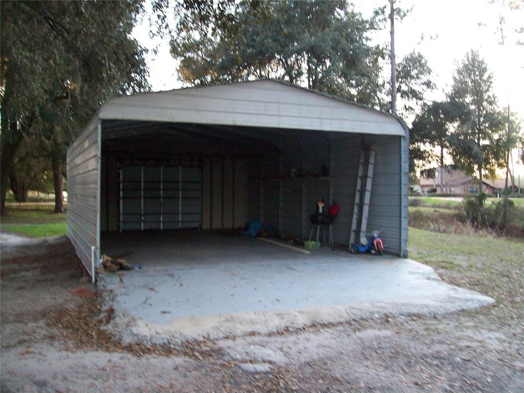 A metal carport with a concrete floor sits on a grassy lot with trees — 6382 BAKER ROAD, KEYSTONE HEIGHTS, FL