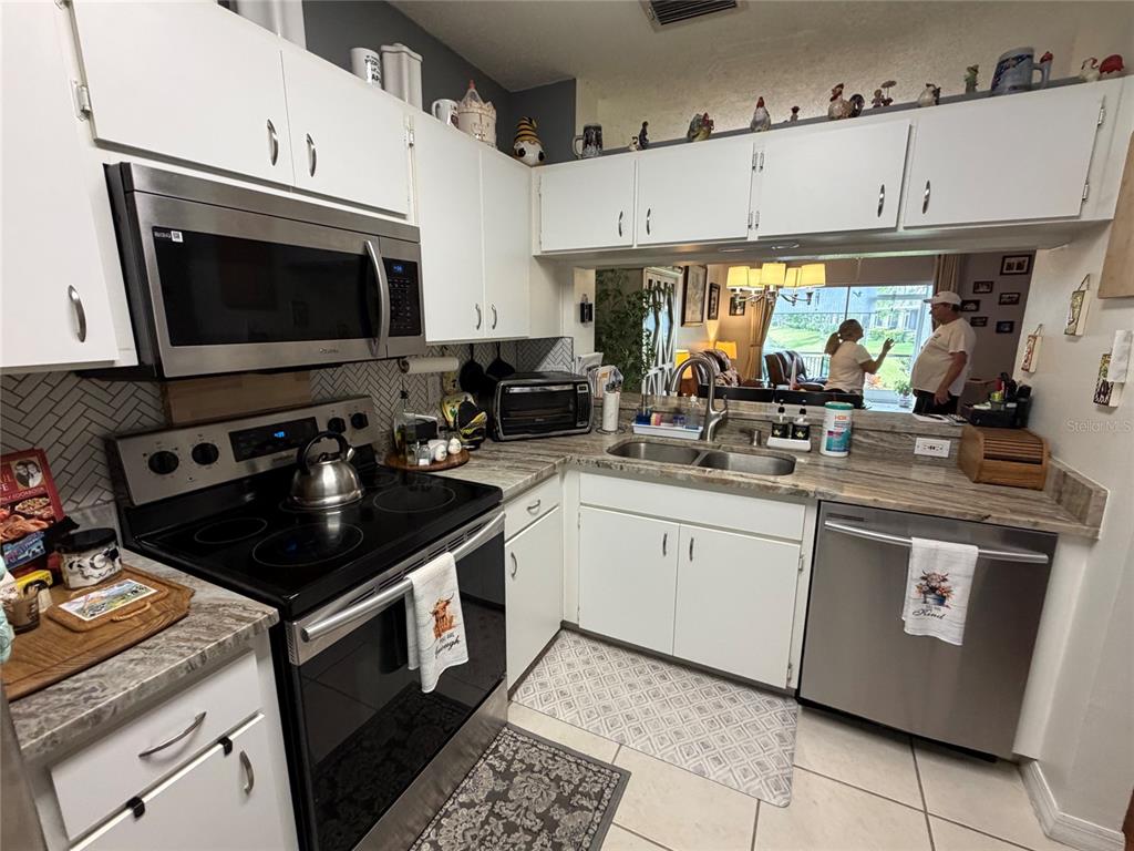 A kitchen features white cabinets, stainless steel appliances, and a pass-through window to the living area — 6211 BAYSIDE KEY DRIVE, TAMPA, FL