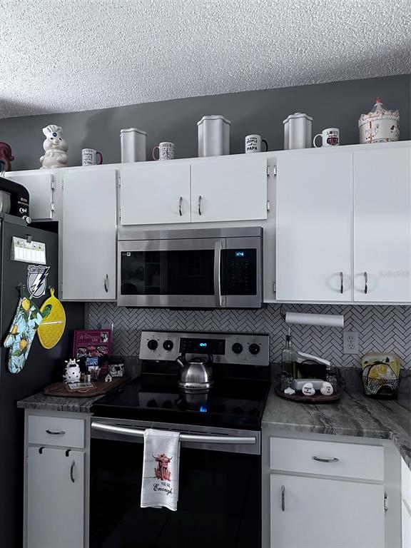 A kitchen features white cabinets, stainless steel appliances, and a gray herringbone tile backsplash — 6211 BAYSIDE KEY DRIVE, TAMPA, FL