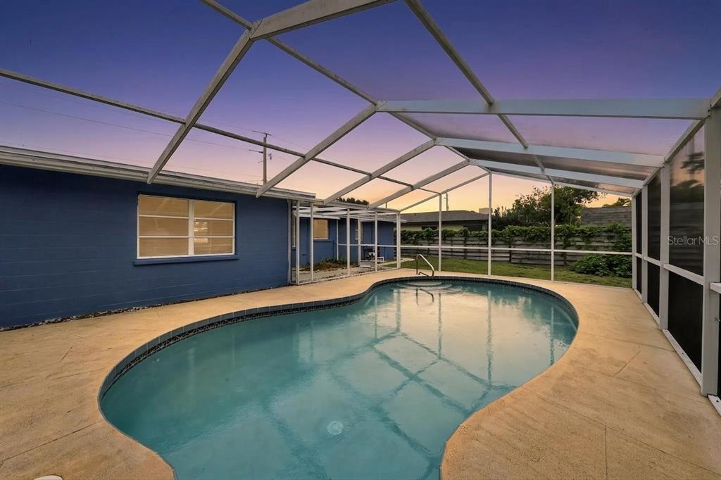 A backyard swimming pool is enclosed by a screened lanai next to a blue house — 3238 SAVAGE ROAD, SARASOTA, FL