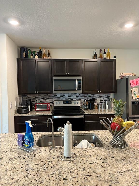 A kitchen features dark wood cabinets, stainless steel appliances, and a granite-topped island with sink — 2015 CHICKASAW BOULEVARD, DAVENPORT, FL