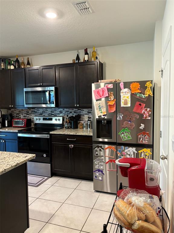 A kitchen features dark wood cabinets, stainless steel appliances, granite countertops, and a tile floor — 2015 CHICKASAW BOULEVARD, DAVENPORT, FL