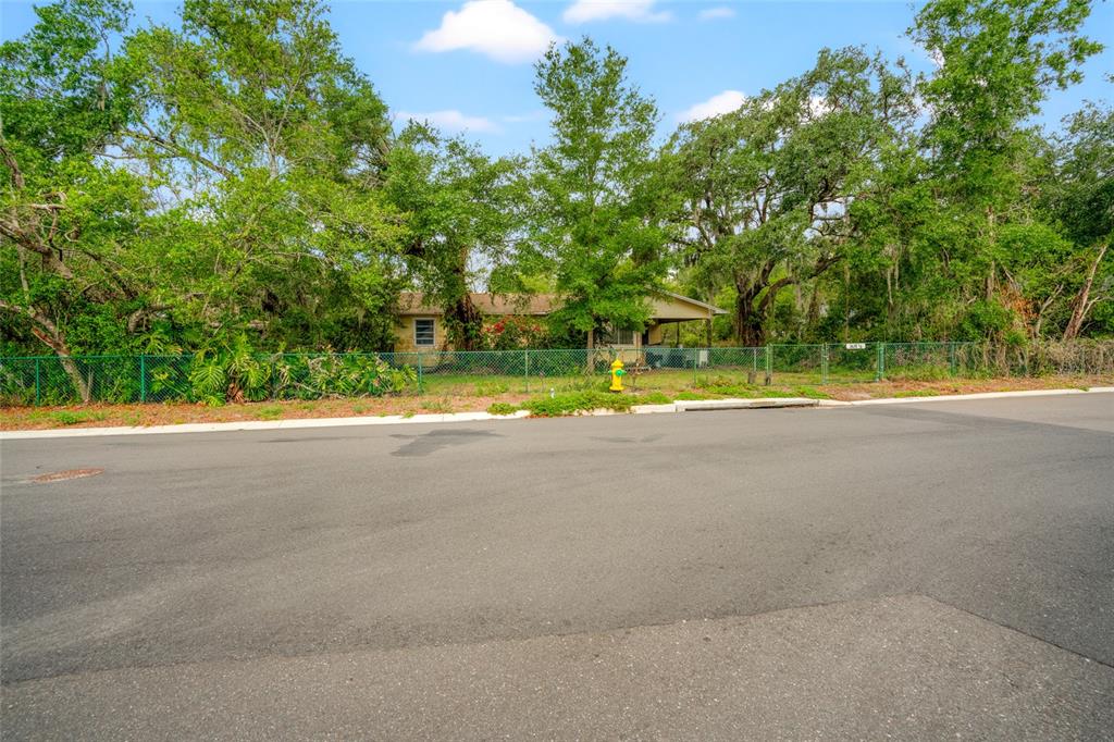 A single-story house sits behind a chain-link fence and mature trees near a street — 3611 W REYNOLDS STREET UNIT 1/2, PLANT CITY, FL