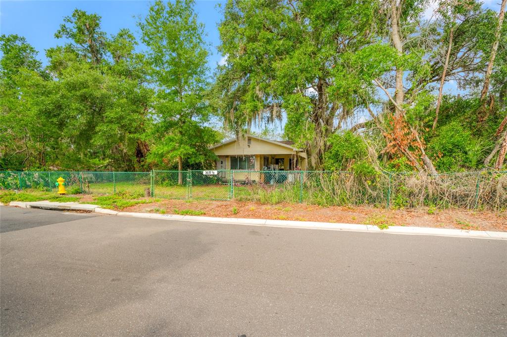 A small, light-colored house sits behind a chain-link fence surrounded by mature trees — 3611 W REYNOLDS STREET UNIT 1/2, PLANT CITY, FL