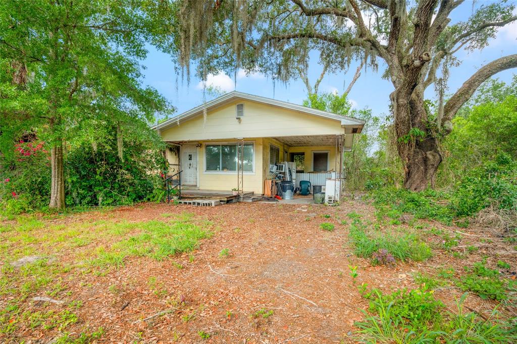 A small, light-yellow house with a front porch sits on a wooded lot — 3611 W REYNOLDS STREET UNIT 1/2, PLANT CITY, FL