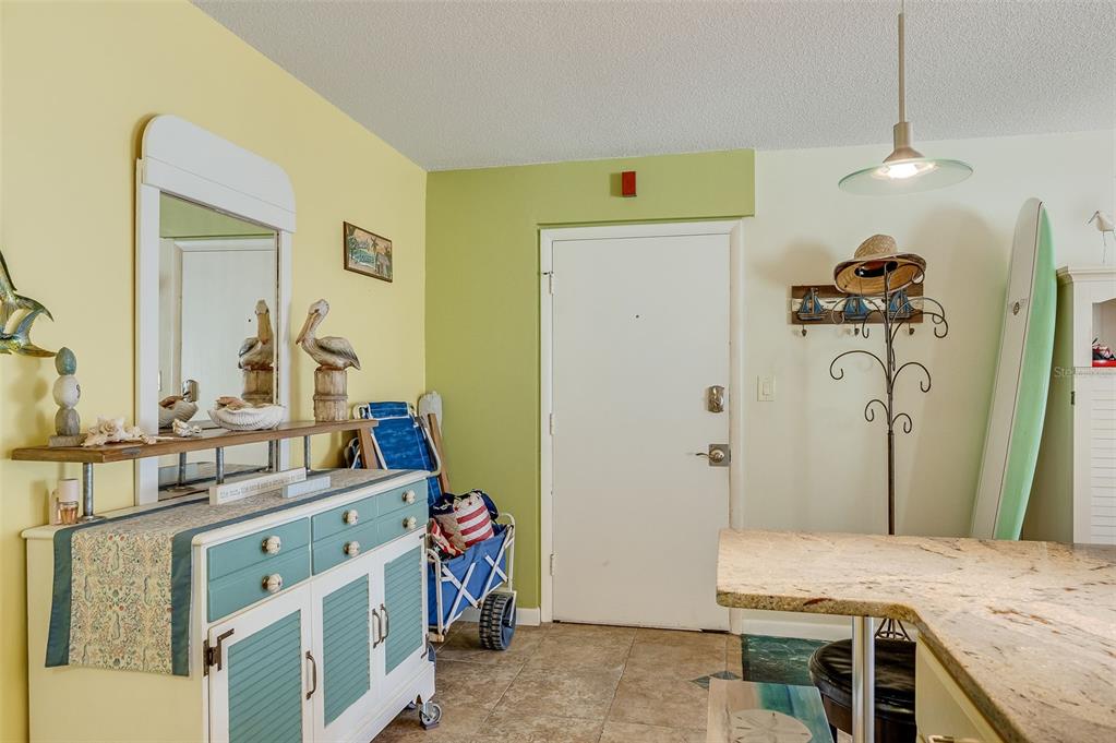 A coastal-themed entryway features a white cabinet, a mirror, and a surfboard leaning against walls — 4800 OCEAN BEACH BOULEVARD UNIT 218, COCOA BEACH, FL