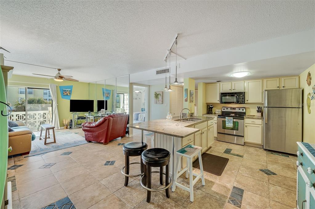 An open-concept kitchen and living area features tile flooring, a granite island, and stainless appliances — 4800 OCEAN BEACH BOULEVARD UNIT 218, COCOA BEACH, FL