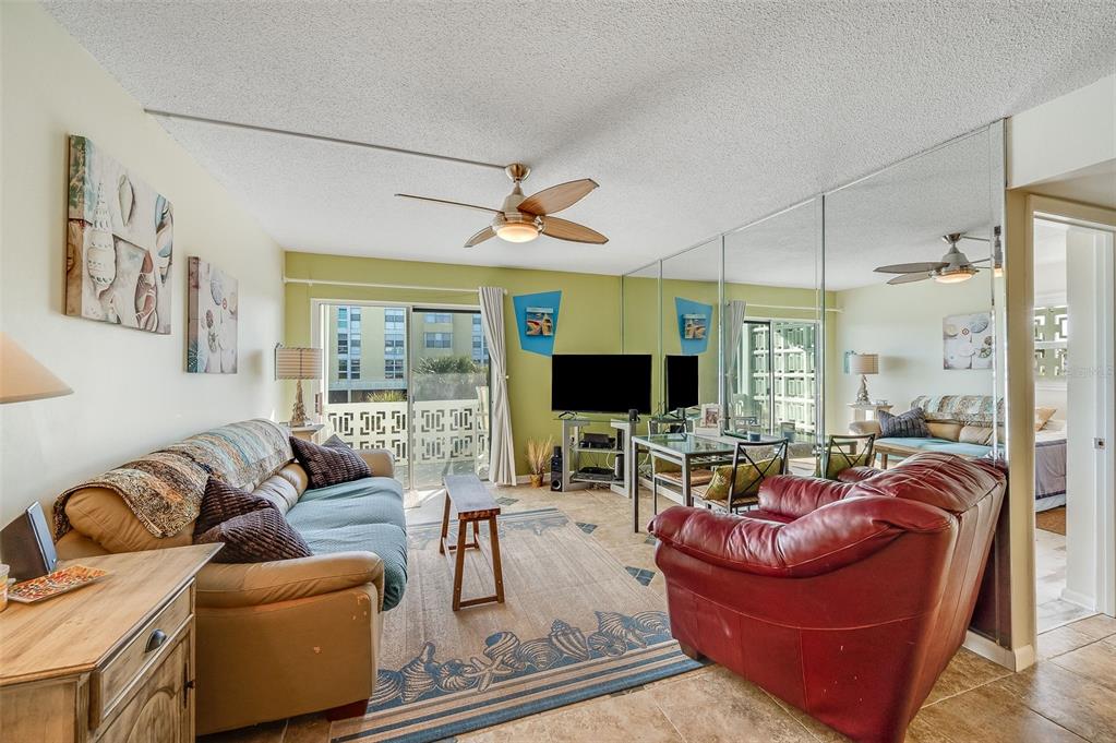 A living room features a tan sofa, red armchair, mirrored wall, and sliding glass doors — 4800 OCEAN BEACH BOULEVARD UNIT 218, COCOA BEACH, FL