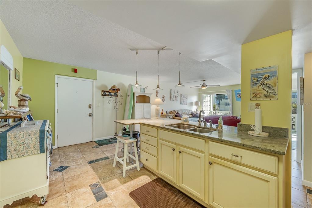 A kitchen with light yellow cabinets and granite countertops opens into a living area — 4800 OCEAN BEACH BOULEVARD UNIT 218, COCOA BEACH, FL