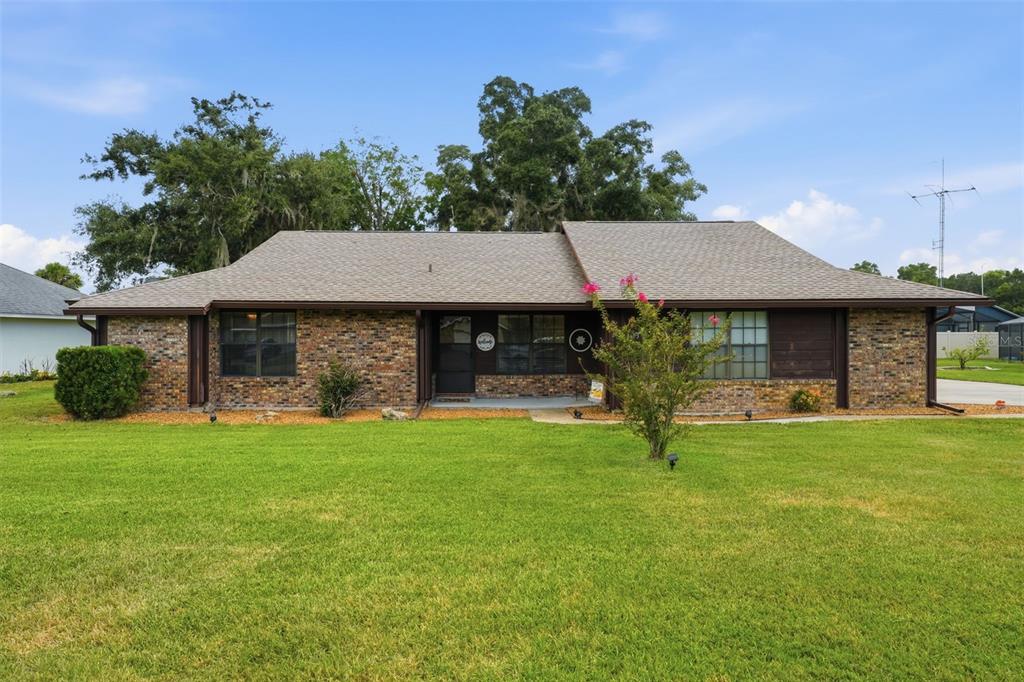 A single-story brick house with a brown shingled roof sits behind a large green lawn — 1805 VIRGINIA COURT, TAVARES, FL