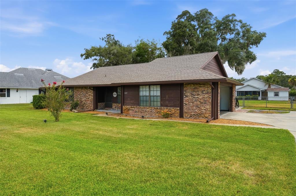 A single-story brick house with a brown roof and attached garage sits on a lawn — 1805 VIRGINIA COURT, TAVARES, FL