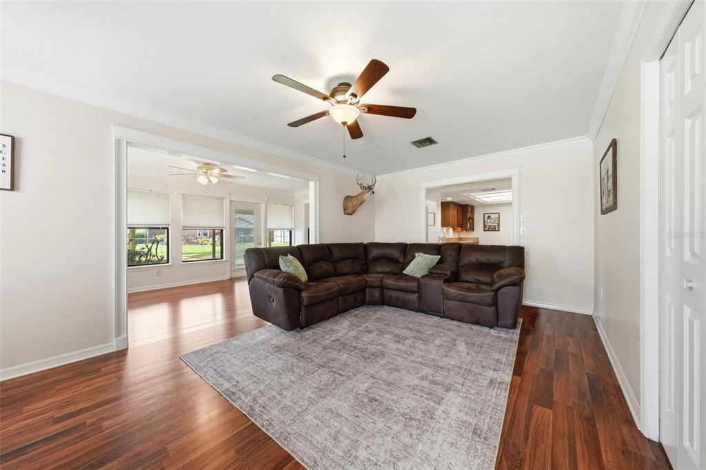 A living room features a brown sectional sofa, a gray area rug, and wood flooring — 1805 VIRGINIA COURT, TAVARES, FL